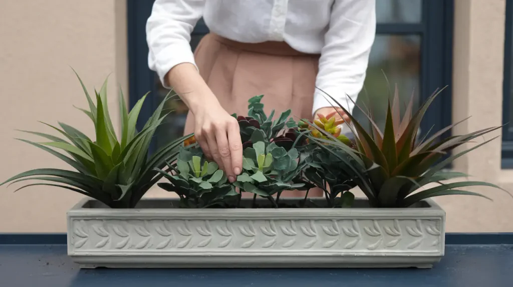 In the living room of 2025, a person tends to potted plants in a rectangular planter on a blue surface, surrounded by an artful mix of real and fake plants.