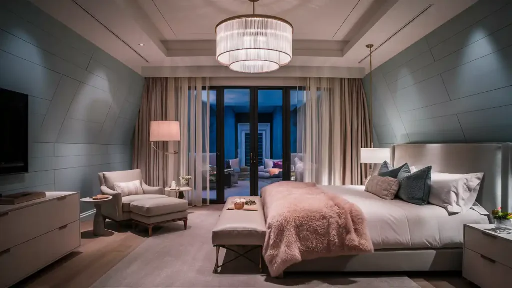A modern bedroom featuring a king-sized bed with a pink throw blanket, armchair with ottoman, bedside tables with lamps, and a large chandelier. Floor-to-ceiling windows with sheer curtains enhance the space. Perfect for activities in home makeover projects.