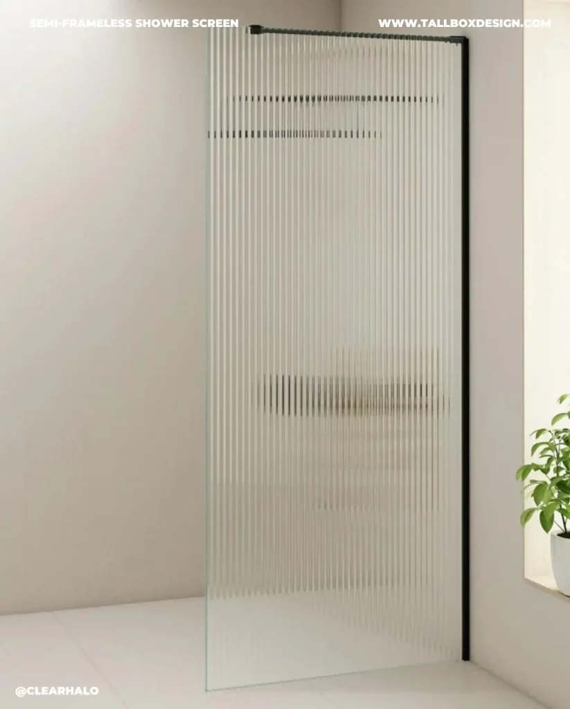 A vertical fluted glass fixed shower screen in a modern bathroom with a small plant in the corner. Text on the glass reads "Semi-Frameless Shower Screen," "ClearHalo," and "TallboxDesign.com.