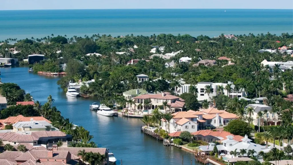 Aerial view of a coastal neighborhood with Waterfront Residences along a canal, numerous palm trees, and the ocean in the background. Ideal for those seeking a prime real estate investment.