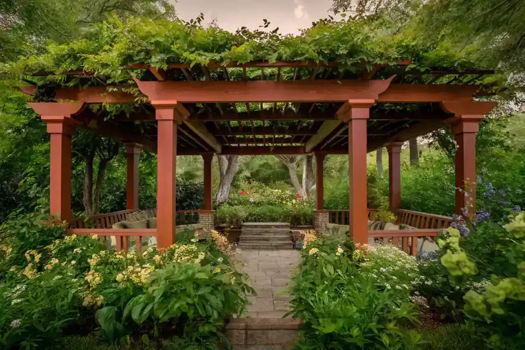 A wooden gazebo surrounded by lush greenery and vibrant flowers with a stone path leading inside creates an inviting atmosphere that can help you sell your home as FSBO.