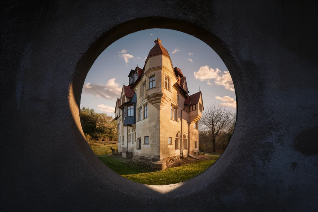View of a medieval castle with red roofs seen through a circular window, under a partly cloudy sky, evoking thoughts.