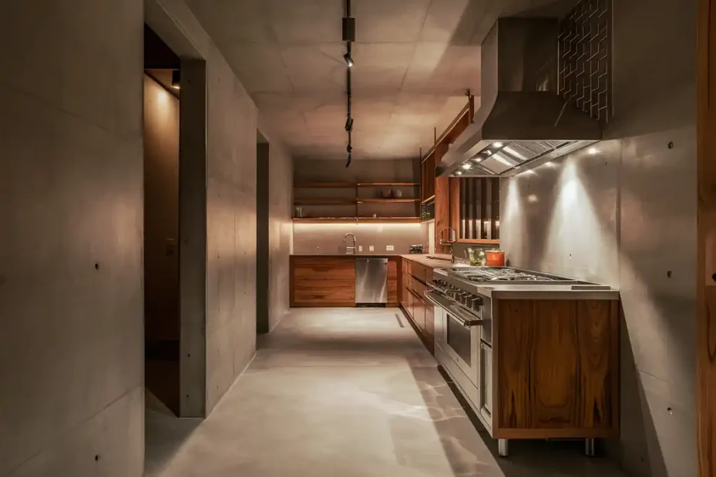 A modern, dimly lit kitchen with stainless steel appliances, wooden cabinets, and a concrete floor seamlessly executed through meticulous pre-construction planning.