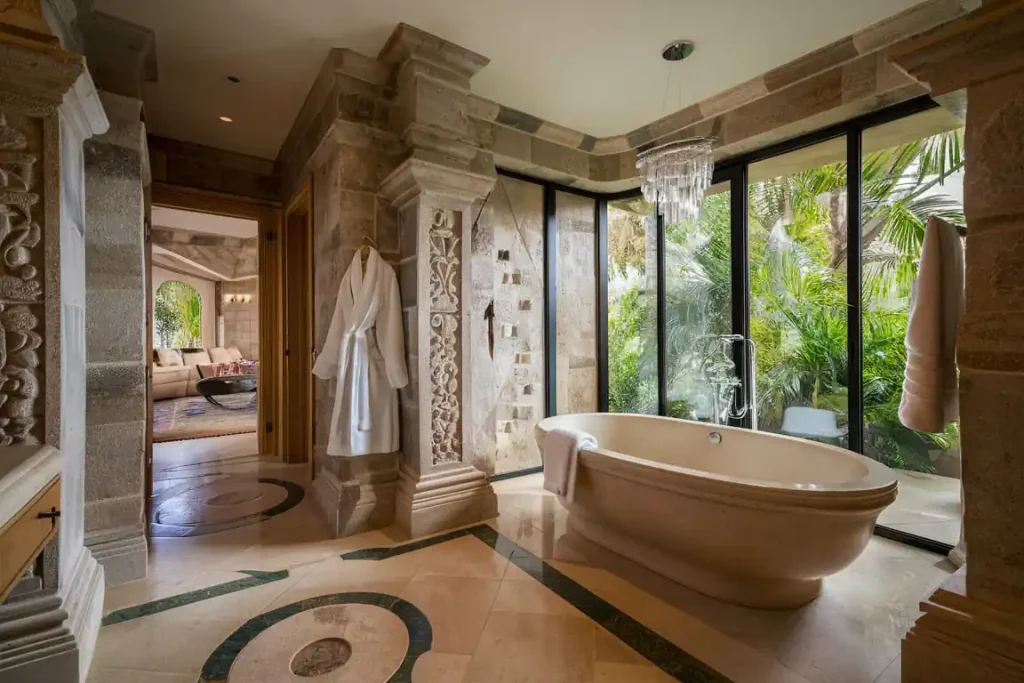 Luxurious bathroom with a freestanding tub, chandelier, stone decor, and large windows opening to a lush garden, reflecting meticulous pre-construction planning.