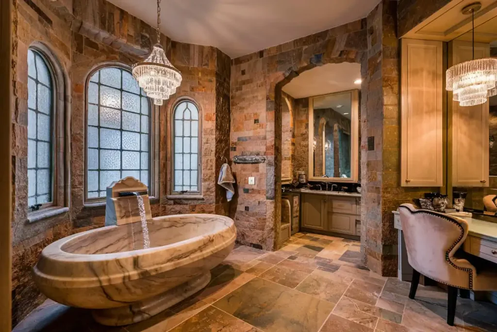 Luxurious stone bathroom with a large marble tub, chandelier, arched windows, and double vanity area, meticulously designed during the pre-construction planning phase.