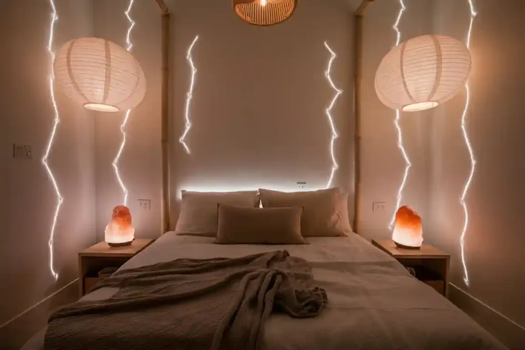 Modern bedroom with ambient lighting, large paper lanterns, and salt lamps on bedside tables framing a cozy, unmade bed.