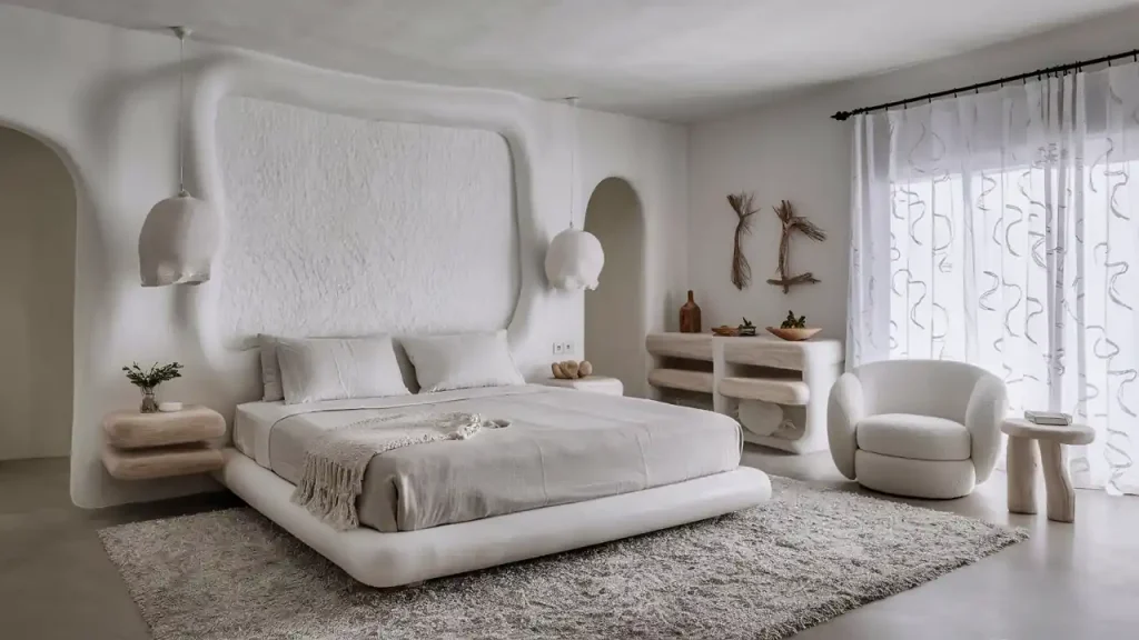 Minimalistic bedroom with a white bed, modern furniture in organic modern style, arched doorways, and a textured wall behind the bed.