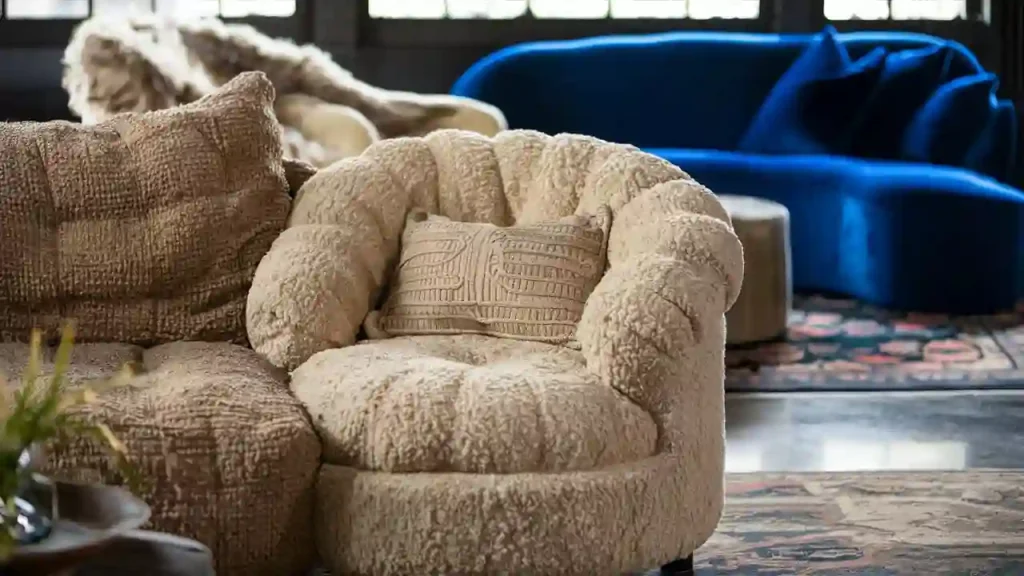 A cozy beige armchair with a textured cushion, set near a matching sofa and a blue sofa, perfectly complements the Organic Modern living room in this well-lit space.