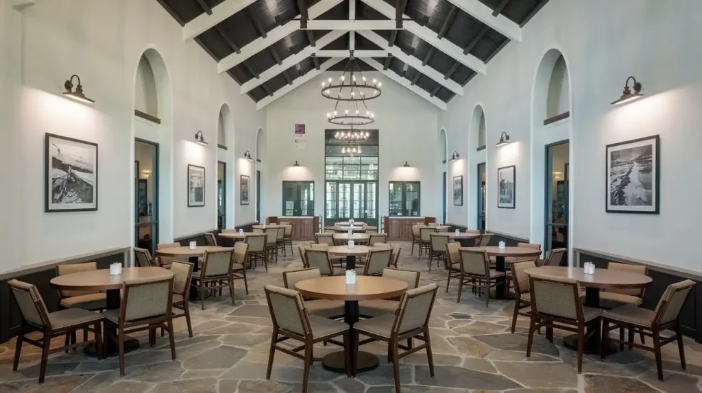 A spacious dining hall with round tables, wooden chairs, black chandeliers, and framed photos on the walls exudes a cozy atmosphere and refined restaurant design.