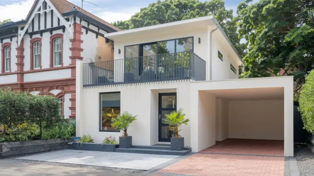 Modern two-story house with a balcony, carport, and a Granny Flat nestled among trees in the background.