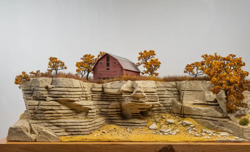 Model landscape featuring a red barn, autumn trees, and rock formations, all nestled beneath a dirt path. This idyllic scene could transform under Class Q regulations or with Permitted Development Rights into a serene residential escape in the countryside.