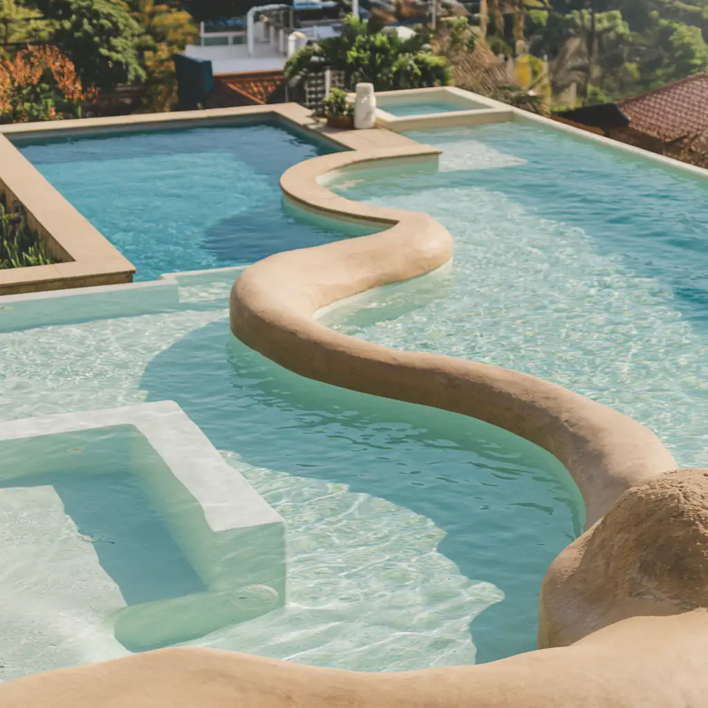 A cascading residential swimming pool with a natural stone design offers stunning scenic hill views in the background.