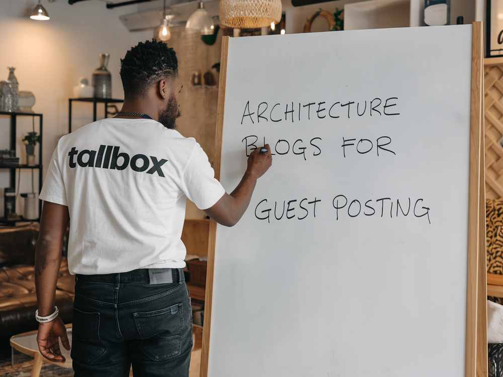In a cozy room, a person is jotting down "Architecture Blogs for Guest Posting" on a whiteboard, channeling innovative ideas for guest blogging that captivates architects and boosts SEO.