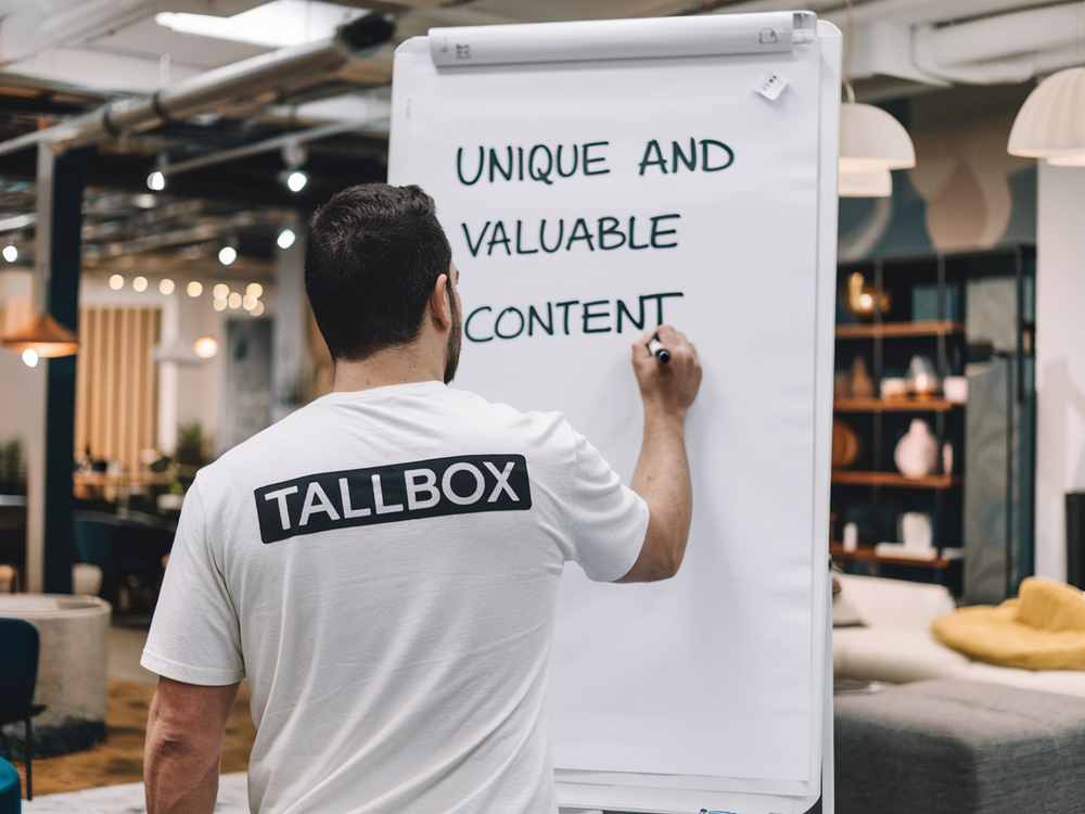 In a modern office setting, a man writes "Unique and Valuable Content" on a flip chart, emphasizing the importance of SEO in crafting compelling narratives.