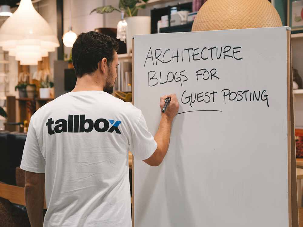 In a store setting, a person scribbles "Architecture Blogs for Guest Posting" on a whiteboard, seamlessly weaving in guest blogging strategies to help architects enhance their online presence and boost SEO efforts effectively.