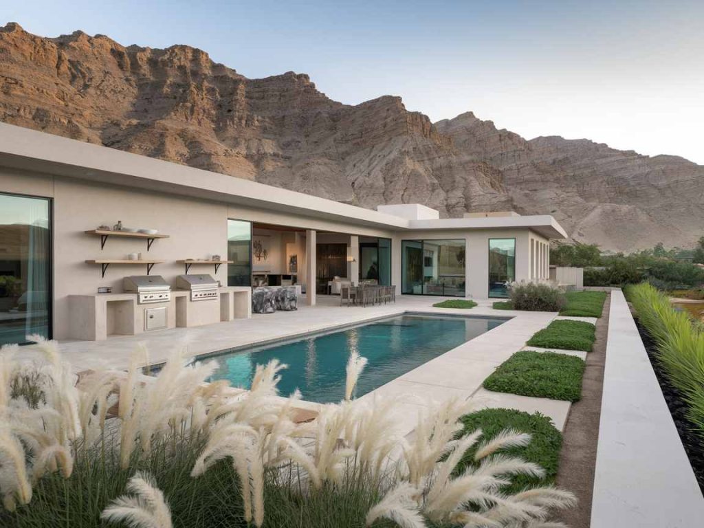 Modern villa with luxury pool ideas, BBQ, and greenery against a backdrop of rugged mountains, enhanced by an inviting outdoor living space.