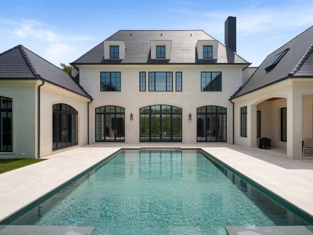 Luxury home with large windows and a stunning swimming pool in the foreground, under a clear blue sky, perfect for enjoying innovative luxury pool ideas and optimizing your outdoor living space.