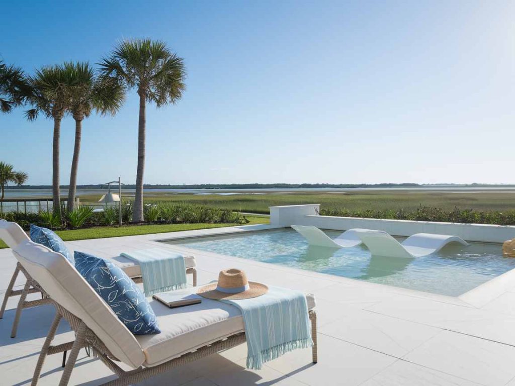 Poolside with chairs and towels, this outdoor living space offers a luxurious experience, overlooking a scenic landscape with palm trees and a clear sky.