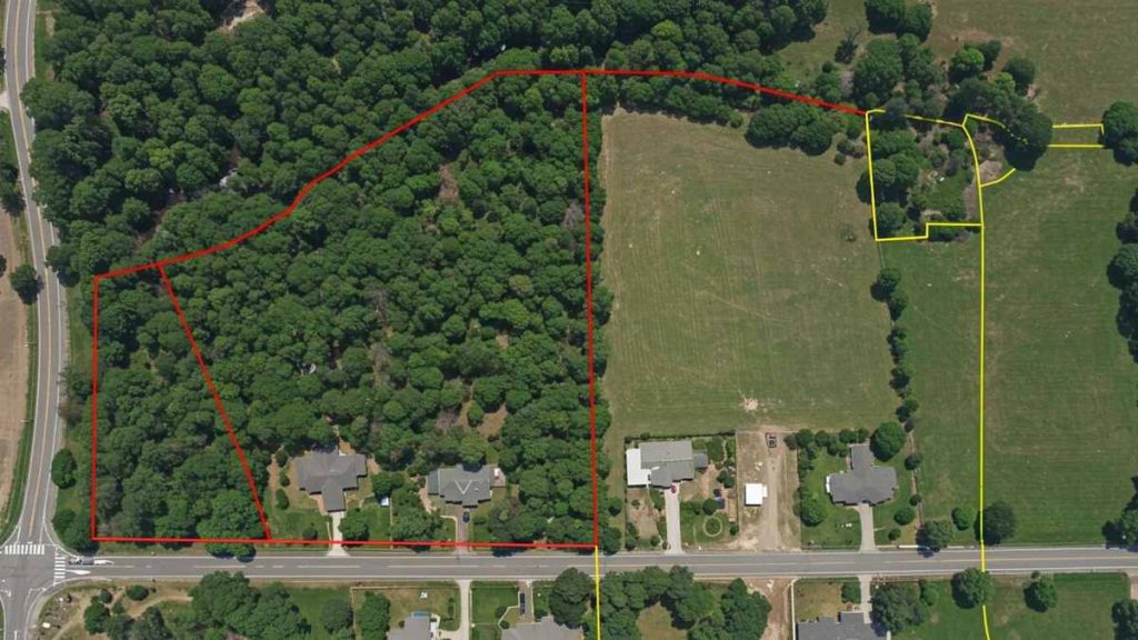 Aerial view of a wooded area bordered in red, with adjacent open fields and residential houses, illustrating a prime opportunity to sell land in the USA.