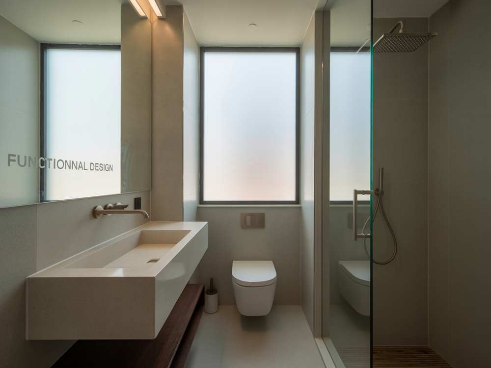 Minimalist bathroom renovation featuring a floating sink, wall-mounted toilet, glass shower, and frosted window—perfect inspiration for your next bathroom remodel.
