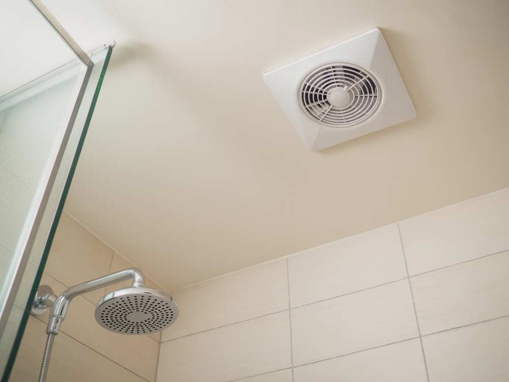 Ceiling exhaust fan above a modern showerhead in a tiled bathroom corner, perfect for avoiding common bathroom renovation mistakes.