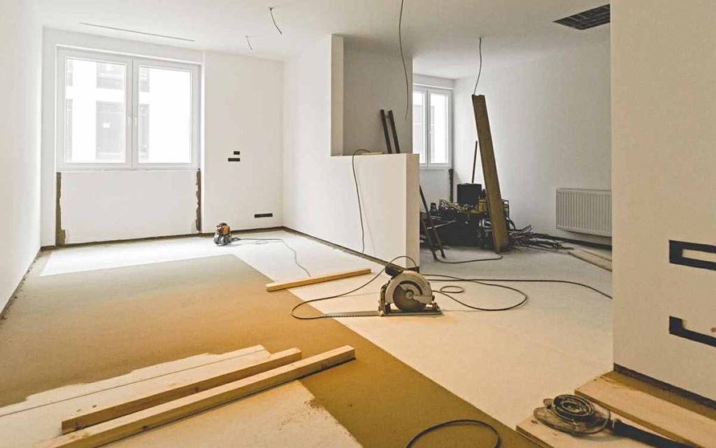 Room under renovation with tools, wooden planks, and exposed wires scattered on the floor, awaiting a thorough post renovation cleaning.