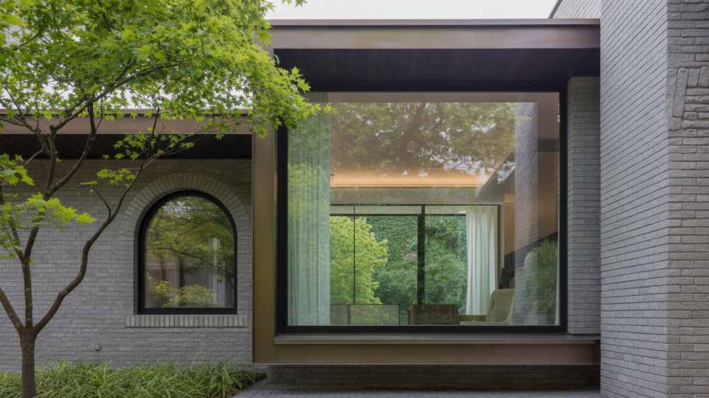 Modern house with large glass window, brick walls, and greenery reflected and visible outside, showcasing innovative architecture and thoughtful design rules.